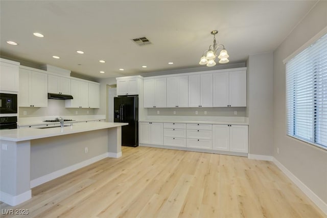 kitchen featuring white cabinetry, sink, hanging light fixtures, black appliances, and light hardwood / wood-style flooring