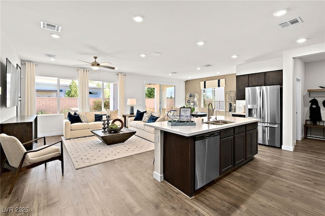 kitchen featuring sink, light hardwood / wood-style flooring, appliances with stainless steel finishes, dark brown cabinets, and a center island with sink