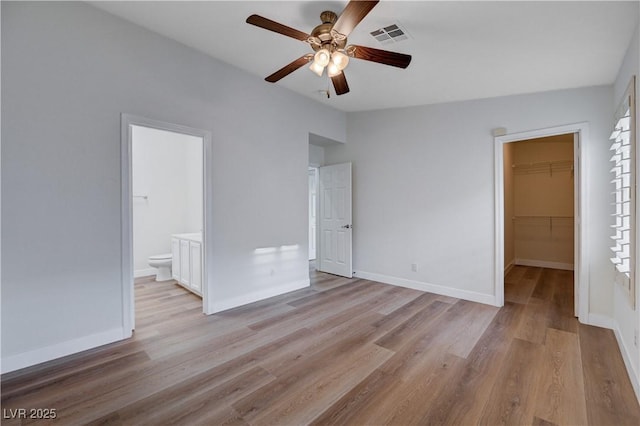 unfurnished bedroom with light wood-type flooring, a walk in closet, ensuite bath, a closet, and ceiling fan