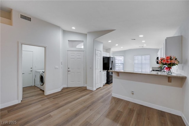 kitchen featuring independent washer and dryer, light wood-type flooring, black refrigerator, kitchen peninsula, and light stone countertops