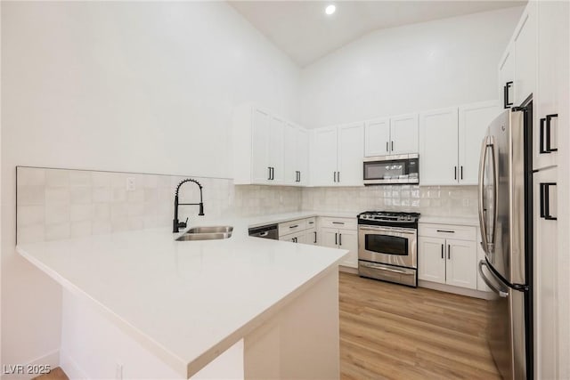 kitchen featuring sink, appliances with stainless steel finishes, white cabinets, kitchen peninsula, and light wood-type flooring