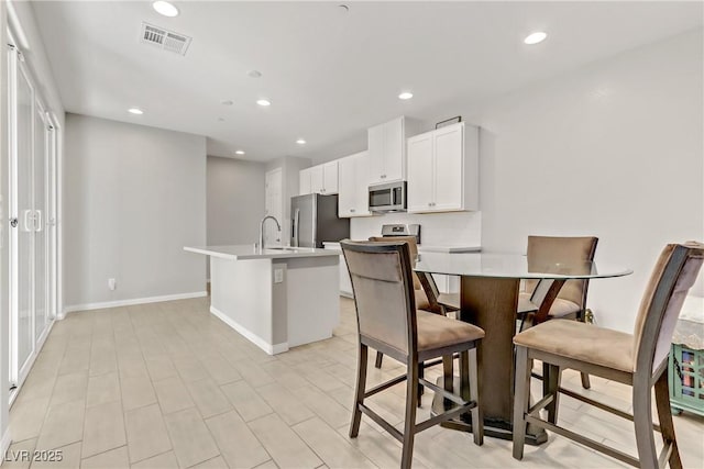 kitchen with appliances with stainless steel finishes, white cabinetry, sink, a kitchen bar, and a kitchen island with sink