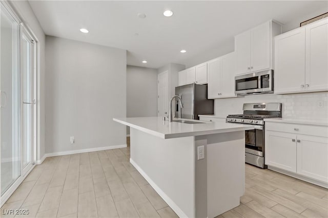 kitchen featuring backsplash, stainless steel appliances, a kitchen island with sink, and white cabinets