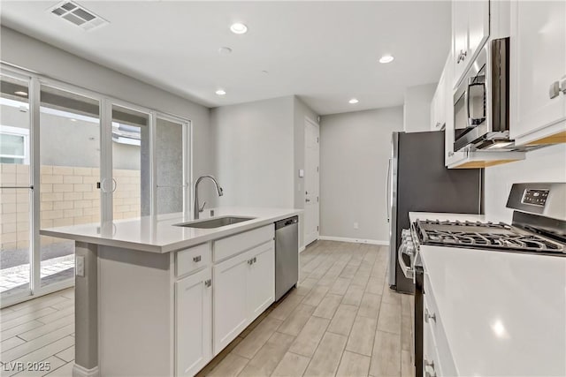 kitchen with stainless steel appliances, white cabinetry, sink, and an island with sink