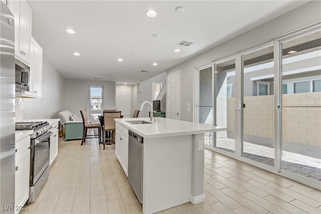 kitchen with stainless steel appliances, sink, a kitchen island with sink, and white cabinets