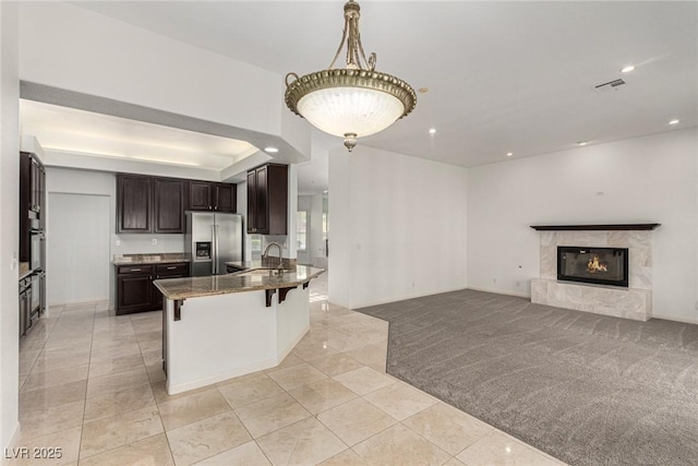 kitchen featuring stainless steel refrigerator with ice dispenser, dark brown cabinetry, a breakfast bar, light carpet, and dark stone countertops