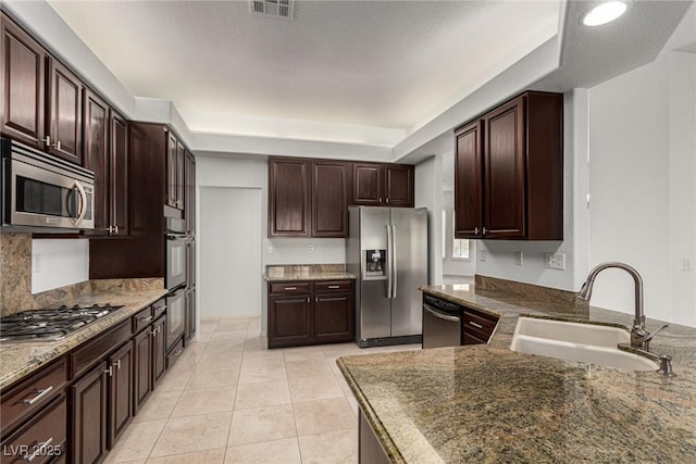 kitchen with stone counters, light tile patterned flooring, appliances with stainless steel finishes, sink, and dark brown cabinetry