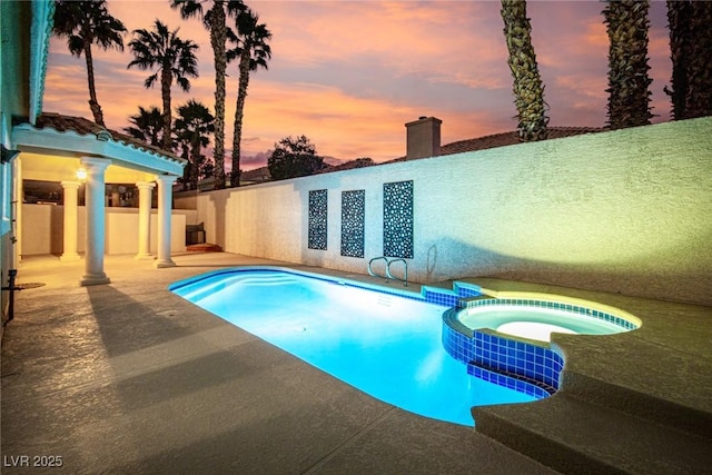 pool at dusk featuring an in ground hot tub and a patio