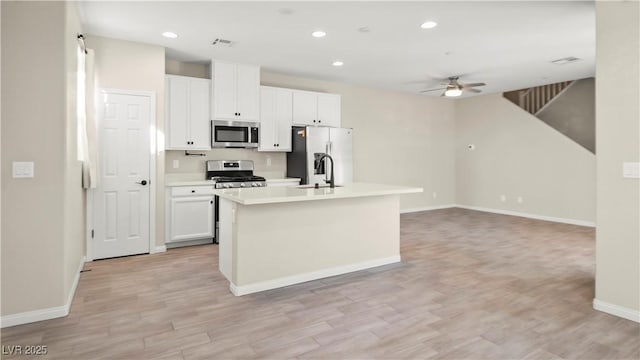 kitchen with appliances with stainless steel finishes, white cabinetry, ceiling fan, light hardwood / wood-style floors, and a center island with sink