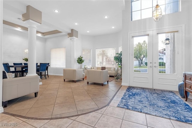 tiled foyer featuring a wealth of natural light, decorative columns, french doors, and a chandelier