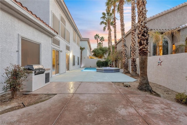 patio terrace at dusk with exterior kitchen, an in ground hot tub, and grilling area