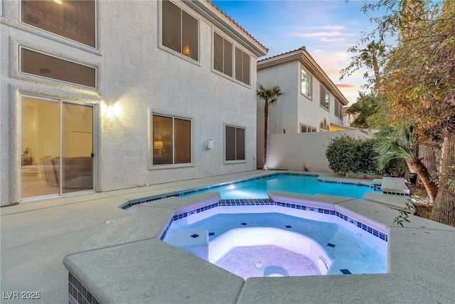 pool at dusk with an in ground hot tub