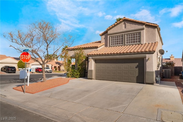 mediterranean / spanish house featuring central AC unit, driveway, an attached garage, stucco siding, and a tile roof