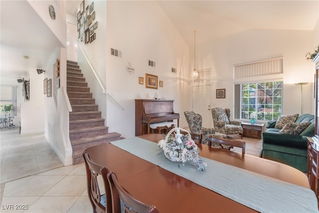 dining space featuring stairway, light tile patterned floors, visible vents, and high vaulted ceiling