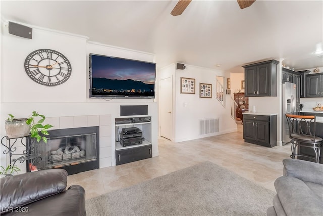 living room with visible vents, a ceiling fan, a fireplace, baseboards, and stairs