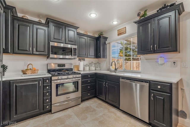 kitchen featuring dark cabinetry, stainless steel appliances, light countertops, and a sink