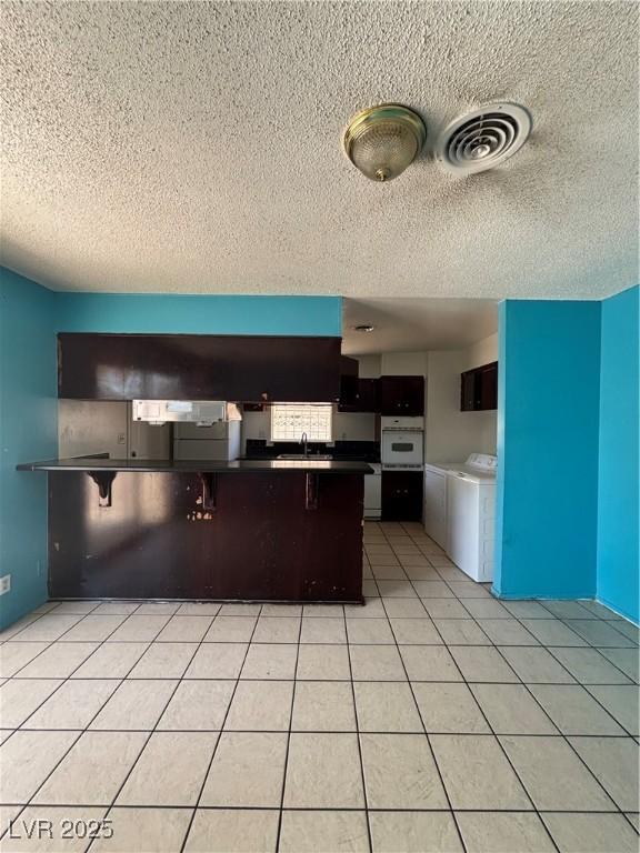 kitchen featuring washer and dryer, a breakfast bar, oven, light tile patterned floors, and kitchen peninsula