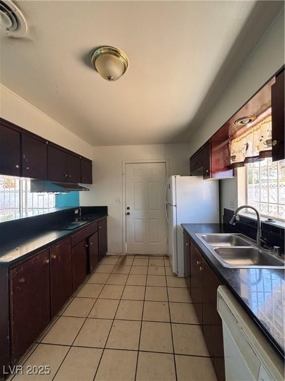 kitchen featuring white appliances, light tile patterned floors, dark countertops, and a sink