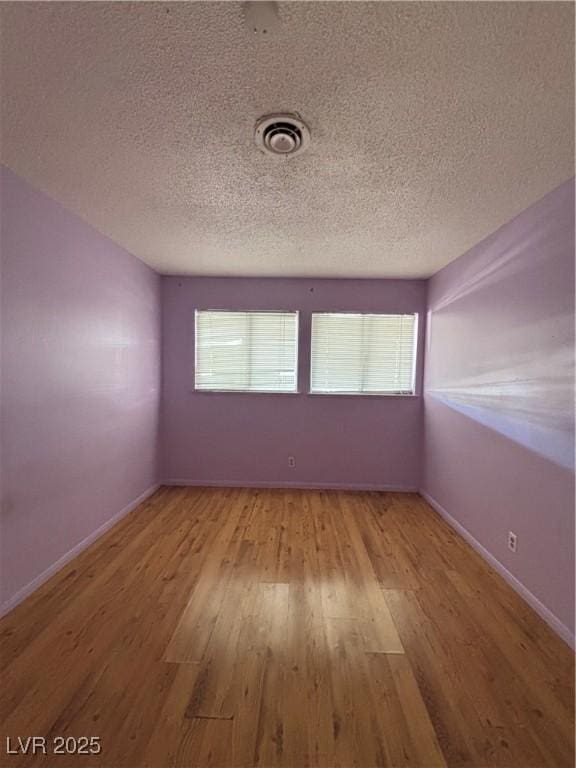 spare room with a textured ceiling, wood finished floors, visible vents, and baseboards