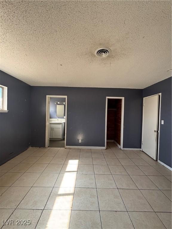 spare room featuring light tile patterned flooring, baseboards, visible vents, and a textured ceiling