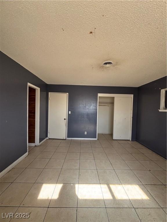 unfurnished bedroom featuring light tile patterned floors, visible vents, a textured ceiling, and a closet