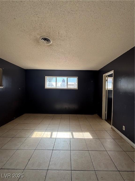 empty room featuring light tile patterned floors, visible vents, and a textured ceiling