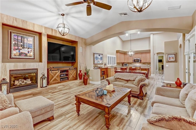 living room with lofted ceiling, ceiling fan with notable chandelier, and light wood-type flooring