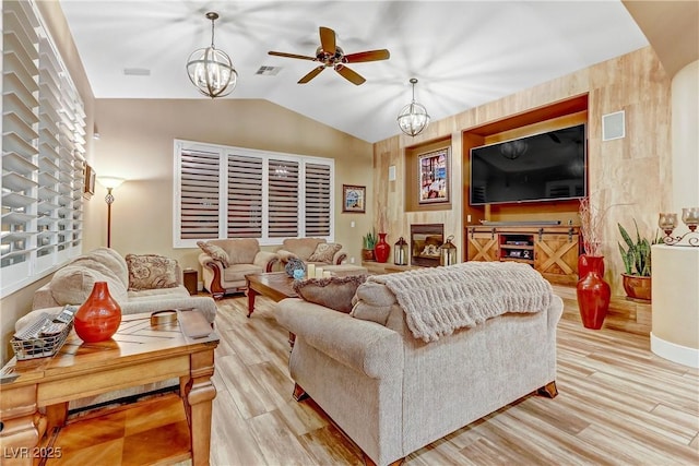 living room featuring vaulted ceiling, ceiling fan with notable chandelier, and light hardwood / wood-style flooring