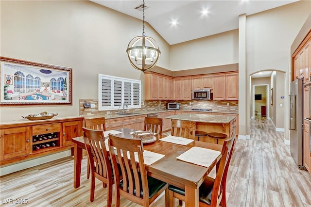 dining room with sink, high vaulted ceiling, a chandelier, and light wood-type flooring