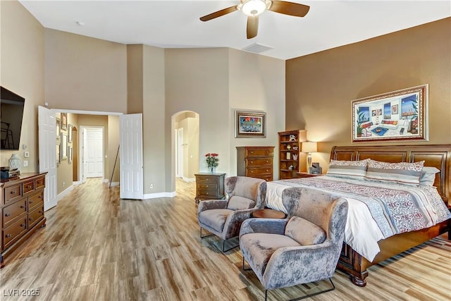 bedroom with a towering ceiling, ceiling fan, and light wood-type flooring