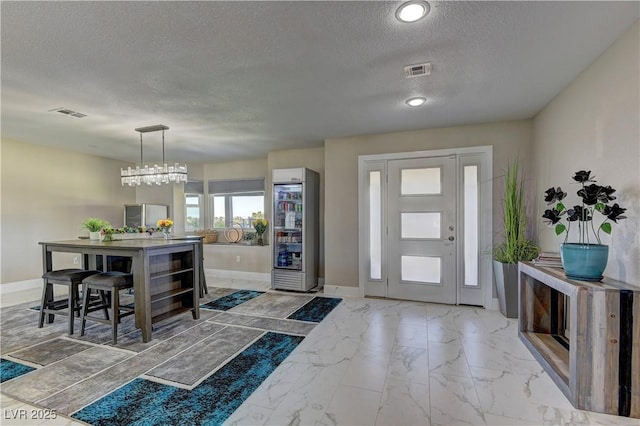 foyer featuring wine cooler, a textured ceiling, and a chandelier