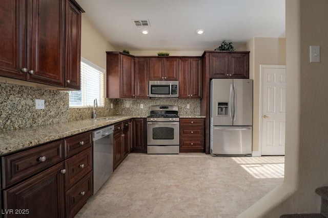 kitchen featuring stainless steel appliances, light stone countertops, sink, and backsplash