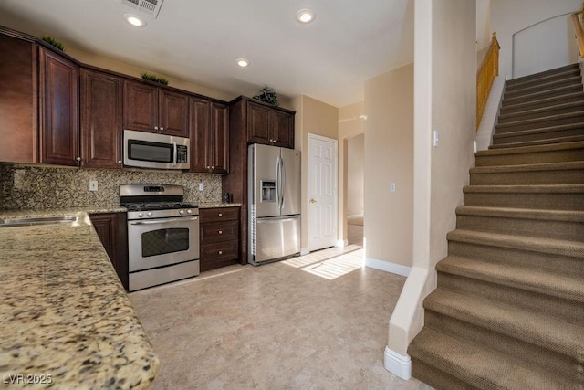 kitchen with appliances with stainless steel finishes, sink, backsplash, light stone counters, and dark brown cabinets