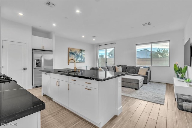 kitchen featuring sink, stainless steel fridge, an island with sink, light hardwood / wood-style floors, and white cabinets