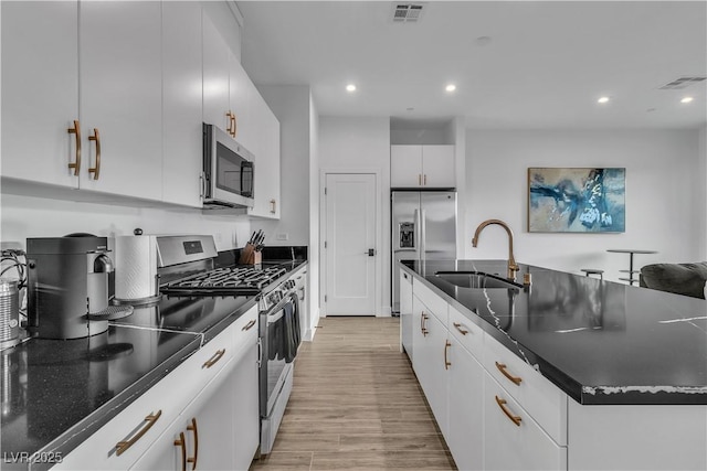 kitchen featuring sink, white cabinetry, a kitchen island with sink, stainless steel appliances, and light hardwood / wood-style floors