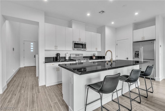 kitchen with sink, a breakfast bar, a kitchen island with sink, white cabinetry, and stainless steel appliances