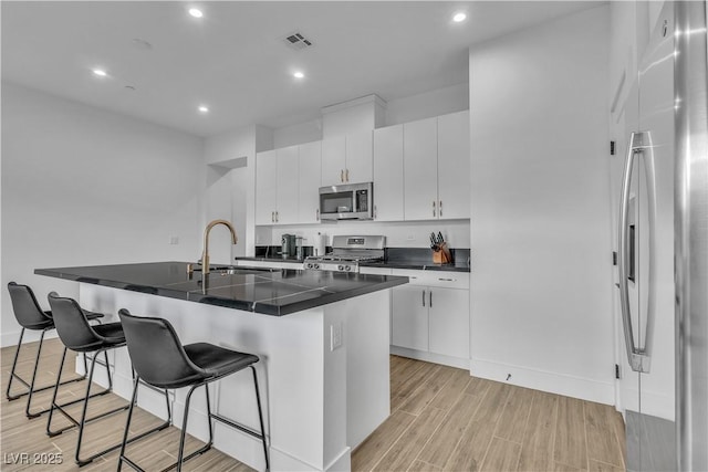 kitchen with white cabinetry, stainless steel appliances, a kitchen bar, and sink