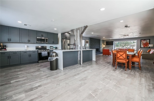 kitchen with gray cabinetry, stainless steel appliances, an island with sink, and light wood-type flooring