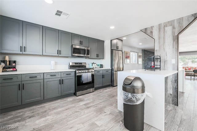 kitchen with a kitchen island, appliances with stainless steel finishes, gray cabinetry, and light hardwood / wood-style floors