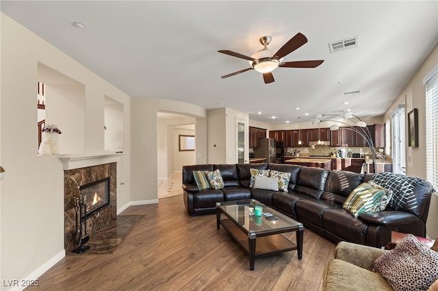 living room with a high end fireplace, light hardwood / wood-style flooring, and ceiling fan