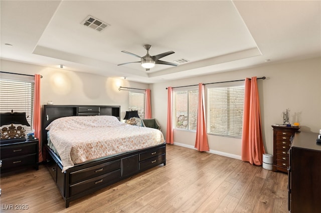 bedroom with a tray ceiling, light hardwood / wood-style floors, and multiple windows