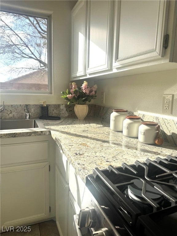 kitchen with light stone counters, gas stove, sink, and white cabinets