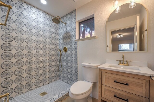 bathroom with a tile shower, vanity, and toilet