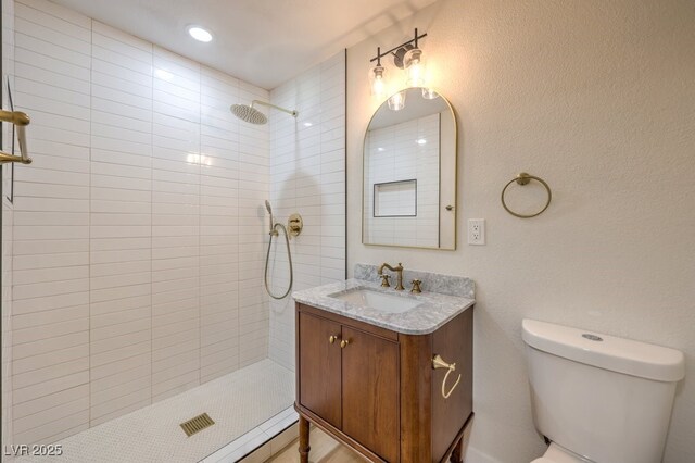 full bath with tiled shower, vanity, and toilet