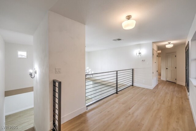 corridor featuring an upstairs landing, visible vents, baseboards, and wood finished floors