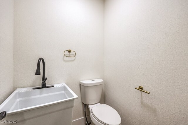 bathroom with a textured wall, a sink, and toilet