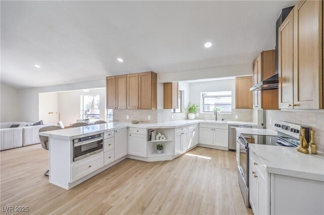 kitchen featuring light wood-style flooring, appliances with stainless steel finishes, open floor plan, a peninsula, and a sink