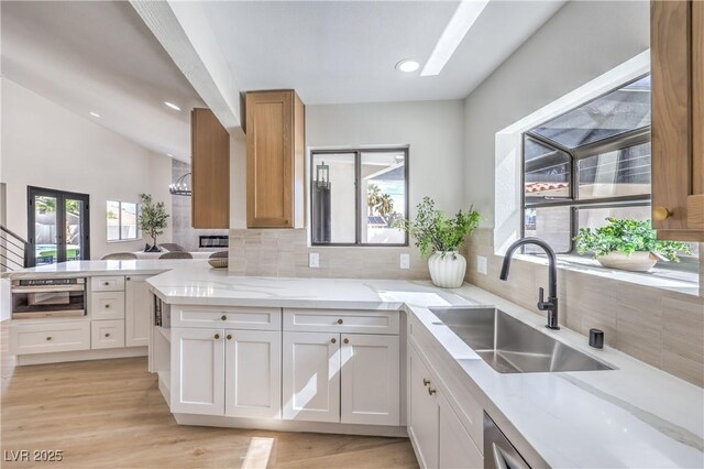 kitchen featuring a peninsula, a sink, light wood-type flooring, decorative backsplash, and light stone countertops