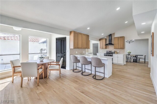 kitchen with a peninsula, a kitchen breakfast bar, light countertops, wall chimney range hood, and stainless steel electric stove