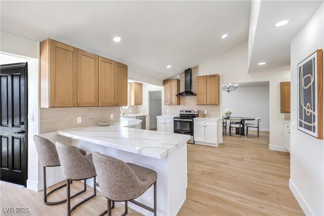 kitchen with a breakfast bar area, light wood finished floors, appliances with stainless steel finishes, light stone countertops, and wall chimney exhaust hood